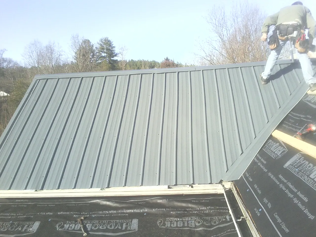 Crew installing dark green standing seam panels over synthetic underlayment in Arcadia