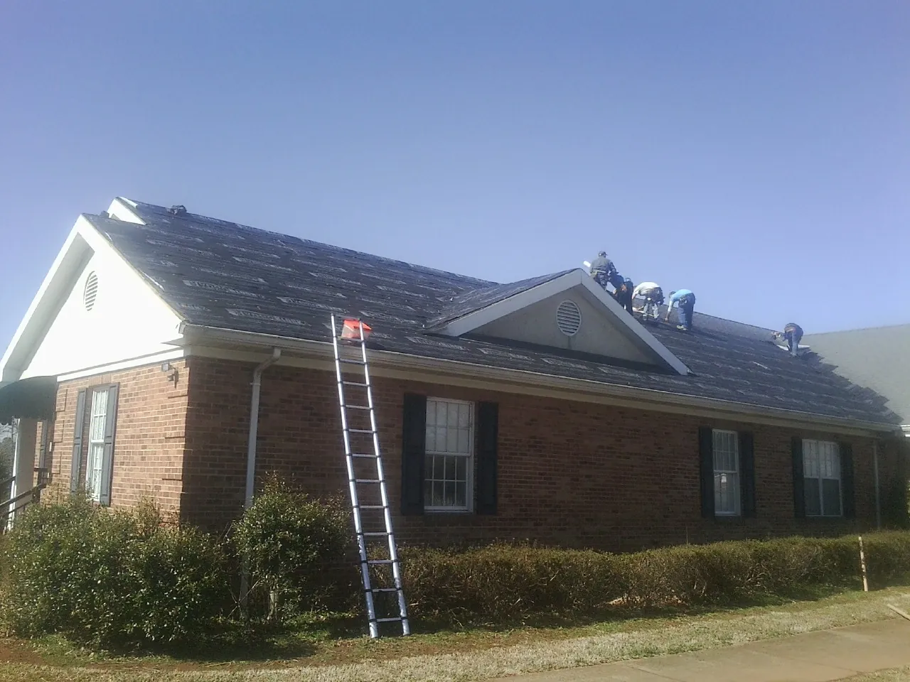 Crew tearing shingles off a brick ranch roof with a ladder set — Emergency Roof Repair work by our crew in Arcadia