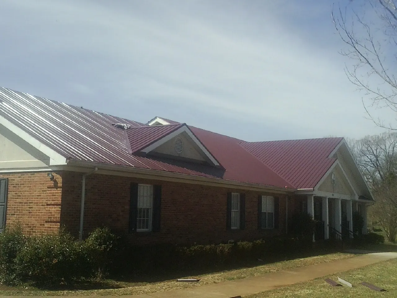 Red metal roof with gabled entries on a long brick building, from a Hail Damage Roof Repair job in Arcadia